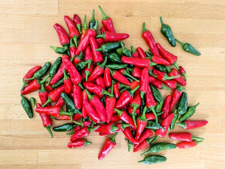 Red and green chilli peppers. Large fresh pile on a wooden kitchen worktop. Overhead view.
