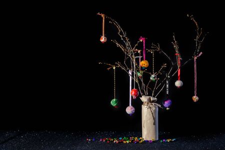 Christmas twig tree table decoration in rustic theme with colourful handmade hanging baubles. Black background and glittery base with jungle bells and copy space.の写真素材