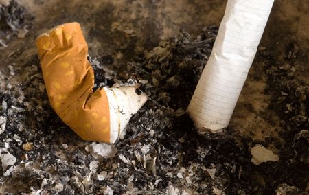 cigarette butts inside an ashtray surrounded by cigarette ashの写真素材