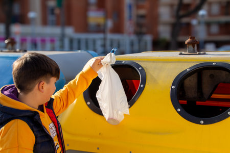 Child recycling plastic bag in colorful recycling bin outdoors.の写真素材