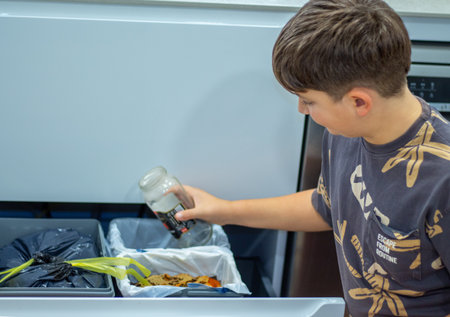 Boy sorting waste into recycling bins in a kitchen.の写真素材