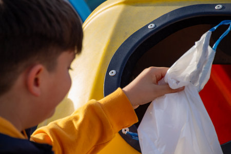Child placing a plastic bag into a recycling bin outdoors.