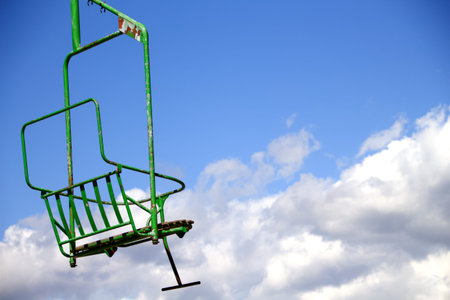 Empty green ski lift chair against a blue sky with clouds.の写真素材