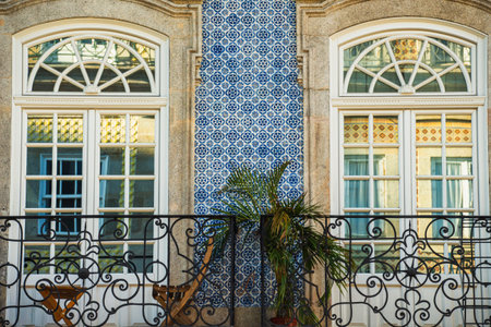 Two elegant windows with decorative iron railings, featuring blue and white patterned tiles in the background, showcasing a blend of architectural styles