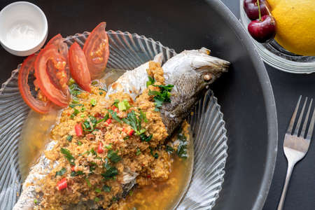 Cooked steamed fish on a plate with ingredients like tomatoesの写真素材