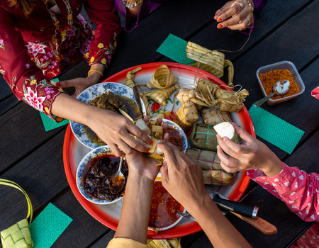 Top view of hands of Muslim family enjoying a variety of traditional Malay cuisines on a circular tray on a black table, at end of Ramadan Mubarak Kareemの写真素材