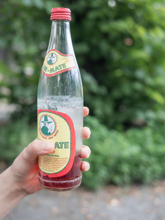 BERLIN, GERMANY - JULY 29, 2017: Hand Holding A Club Mate Pomegranate Bottle With Tree In The Backgroundのeditorial素材
