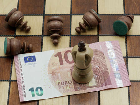 Money Rules Concept: King Chess Piece Standing On A 10 Euro Banknote With Defeated Lying Pawns On A Chess Boardの写真素材