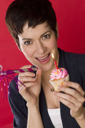 A woman smiles before blowing out her candle and eating her cupcakeの写真素材
