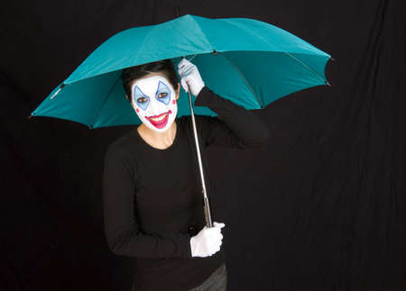 A happy clown shelters under a colorful umbrellaの写真素材