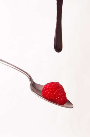 Raspberries on a spoon with chocolate syrup dropping on themの写真素材