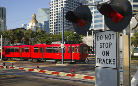 Downtown Scene at RailRoad Crossing Red Trolley Car Passing Signal Lights with Buildings in the Backgroundのeditorial素材