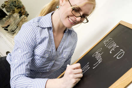 Beautiful Female Teacher Writes a Message on ChalkBoard Saying Welcome to Biologyの写真素材