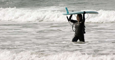 Surfer female in full wertsuit carries board back to shore on the Oregon Coast