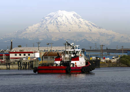 A Tugboat returns to dock after guiding a container ship out to sea Mt. Rainier in backgroundのeditorial素材