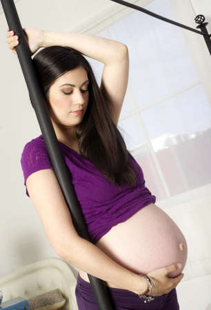 Woman expecting a baby holds canopy bed standing in front of windowの写真素材