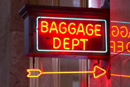 A red neon sign points the way to the baggage depot in the train stationの写真素材