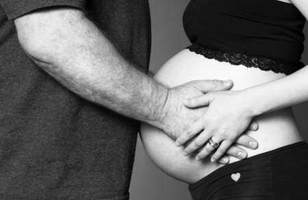 Pregnant woman standing touches belly with manの写真素材
