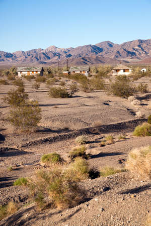 Dry ground and sage brush inhabit the foreground with abandoned buildings in the backgroundの写真素材