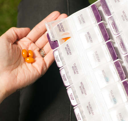 Pills are poured into hand from the daily weekly medication planner holderの写真素材