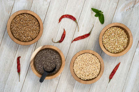 Wheat Berries Buckwheat Groats Pearl Barley Chia Seeds in Bowls with Red Peppers on the sideの写真素材