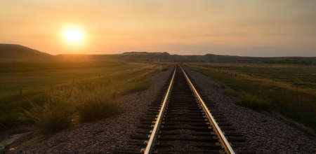 The sun comes up revealing a transportation themed image with train tracksの写真素材