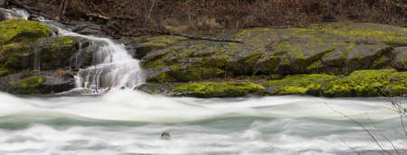 Whitewater flows fast over and past rocks and green moss in the Umpqua Riverの写真素材
