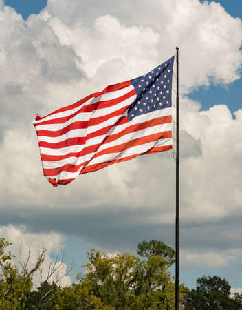 The sun hits an United States American flag as it waves in the wind against a partly cloudy skyの写真素材