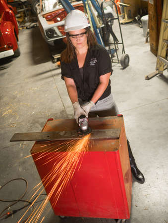 Sparks fly as this young woman grinds a piece of metal in the hot rod shopの写真素材