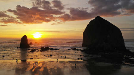 People walk on the beach reflection late afternoon at dusk in Cannon Beach Oregon