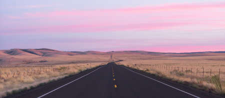 Pink light engulfs the sky at dawn over the long lonely highwayの写真素材