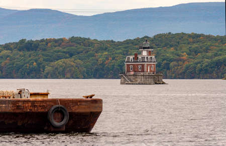 A rusty old barge sits in the foreground near the Hudson Athens Lighthouse in Upstate New York USA