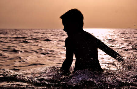 Child Silhouette Splashing Water over Sunset in the Sea
