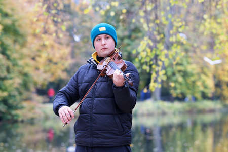 Boy playing a violin on lakeshore in the park