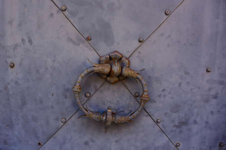 Vintage metal door handle on a old grey metal door with a x shape and golden details