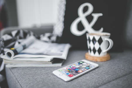 White mobile phone lying on a couch with cup and stack of magazines