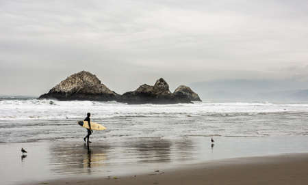 Man Carrying Surfboard in Front Bodies of Water on Brown Sand