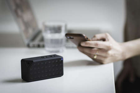 Person Holding Iphone Beside Black Portable Speaker