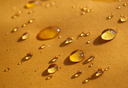 Water drops over a dark yellow surface, lit by sunlight.の写真素材