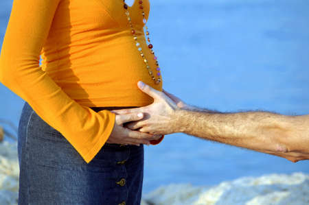 Detail of male arm and hand, touching pregnant woman's belly with care.