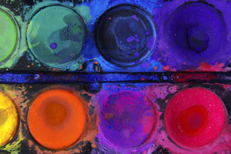 Closeup of messy, used water-color paint-box with black background.の写真素材