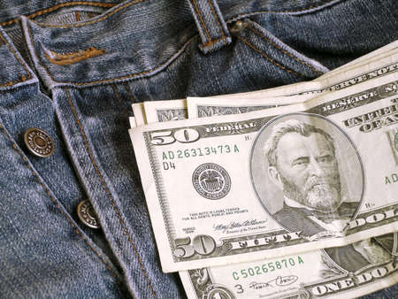 Dollar banknotes over old blue jeans

