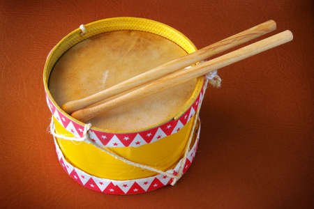 Old yellow drum toy with drum sticks over brown leather backgroundの写真素材