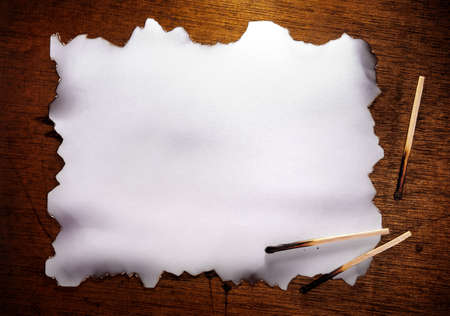 Piece of blank paper with burned edges and matches over a wooden backgroundの写真素材