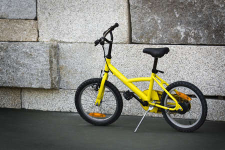 Single yellow bicycle on walkway against a stone wallの写真素材