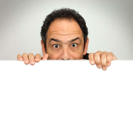 Shocked man peeking behind a blank white billboardの写真素材