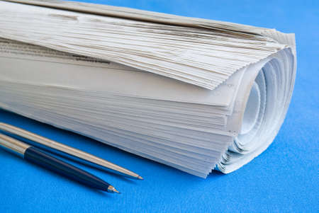 Closeup of a newspaper roll on a blue table with two pens by the side の写真素材