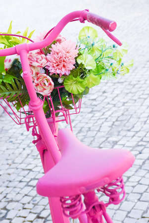 Detail of a pink painted bicycle with a basket with flowers and leaves Detail of a pink painted bicycle with a basket with flowers and leaves