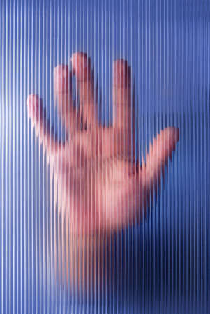 A male hand pressing on a hazy and striped glass window の写真素材