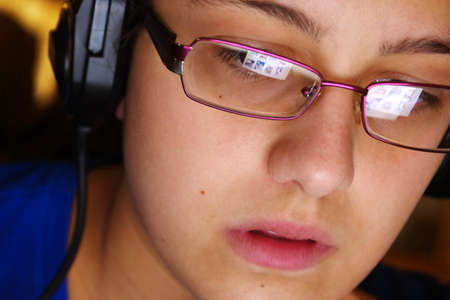 Hi-tech youth concept with a young girl using headphones and glasses reflecting her computer screenの写真素材